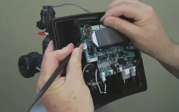 Technician with multimeter probing water softener control board circuit — diagnosing dead control head, drive motor or display failure