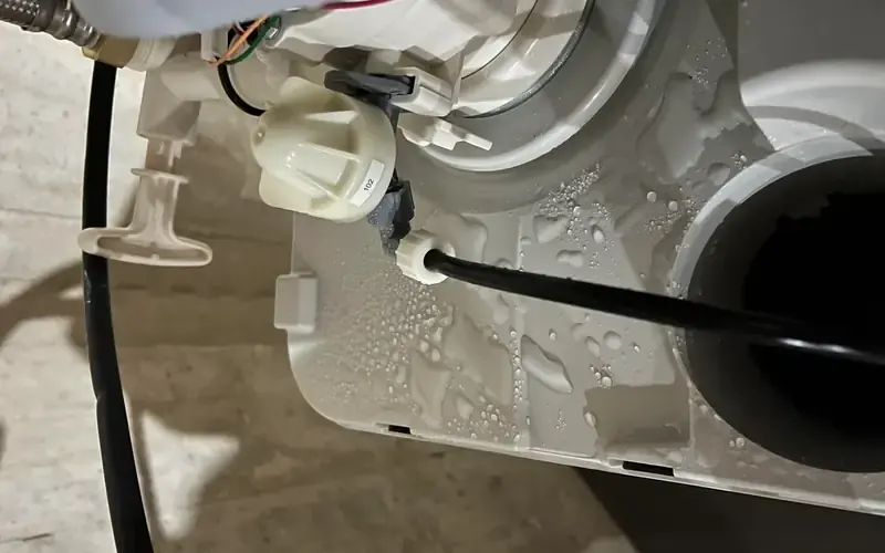 Water leaking from softener control valve onto basement floor — wet base, water droplets on bypass and tubing visible